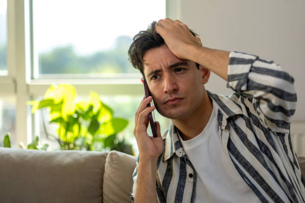 istock Young man looks confused while talking on the phone at home 2167957501