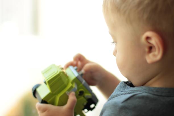 A small serious boy plays calmly with a green car