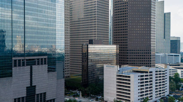 Towering skyscrapers define downtown Houston skyline, showcasing a mix of architectural styles. Glass-clad office buildings reflect the sky, while concrete structures add depth to the urban landscape. C. Baldwin Hotel stands prominently among the high-rises. Multi-level parking structure and green space in the foreground provide contrast to the vertical cityscape, capturing the essence of Houston's bustling business district.
