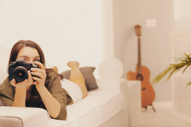 istock Young woman relaxing on couch taking photos with camera 2167966669