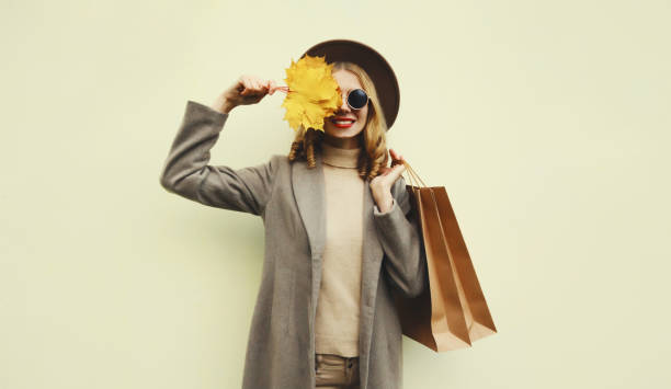 Autumn portrait of beautiful happy woman with shopping bag, stylish girl holding yellow maple leaves stock photo
