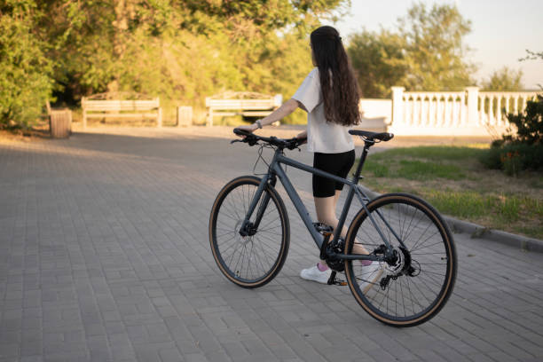 istock woman in a white shirt walks alongside a black bicycle on a brick path with a bench and a city view in the background, lit by the setting sun 2167967681