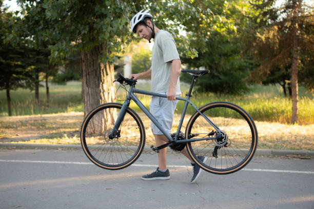 istock man walks on a paved path in a park, carrying a black bicycle over his shoulder 2167967961