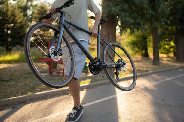 istock man walks on a paved path in a park, carrying a black bicycle over his shoulder 2167967982