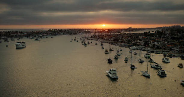Aerial shot of Newport Beach, an affluent coastal city in Orange County, California on a cloudy summer evening, looking out towards the sun as it sinks below a bank of cloud towards the Pacific Ocean. \n\nAuthorization was obtained from the FAA for this operation in restricted airspace.