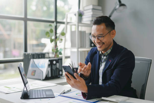 istock Cheerful asian businessman is using a smartphone and laptop for a video conference call while working in the office 2167985088