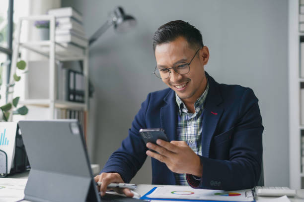 istock Asian accountant is smiling while working in his office, using a smartphone and a tablet 2167985108