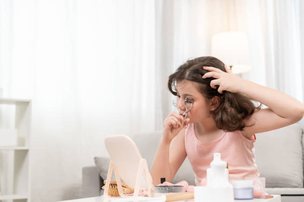 istock curling eyelashes. Happy children sit in front of a mirror makeup on face Advertisement, lifestyle , cosmetics, makeup accessories, beauty activity, beautician, talent, love beauty 2167989740