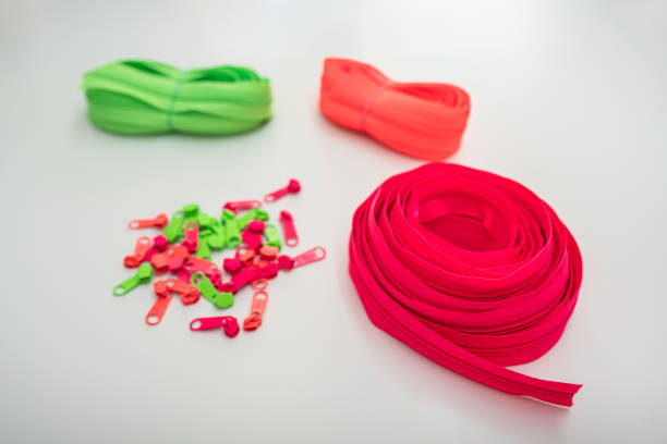 Three brightly colored zipper rolls, in neon green, orange, and pink, are laid out on a white surface alongside matching zipper sliders in green, pink, and orange. The vibrant colors create a playful and creative atmosphere, ideal for sewing or fashion projects.