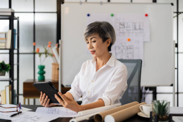 istock A female architect reviews architectural plans on her tablet while sitting at her desk, with various design sketches and tools around her in a modern, well-organized office 2168012371