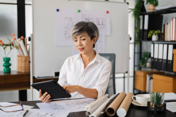 istock A female architect reviews architectural plans on her tablet while sitting at her desk, with various design sketches and tools around her in a modern, well-organized office 2168012374
