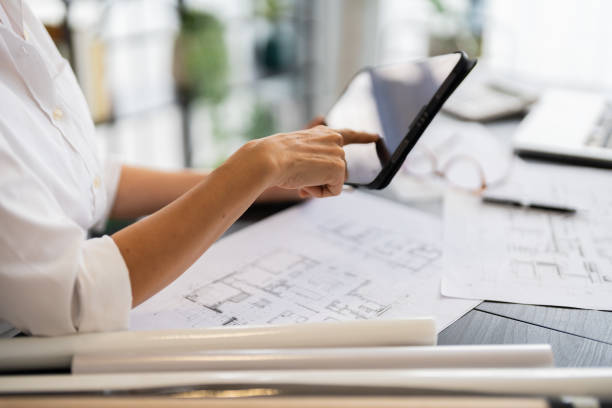 istock A female architect reviews architectural plans on her tablet while sitting at her desk, with various design sketches and tools around her in a modern, well-organized office 2168012381