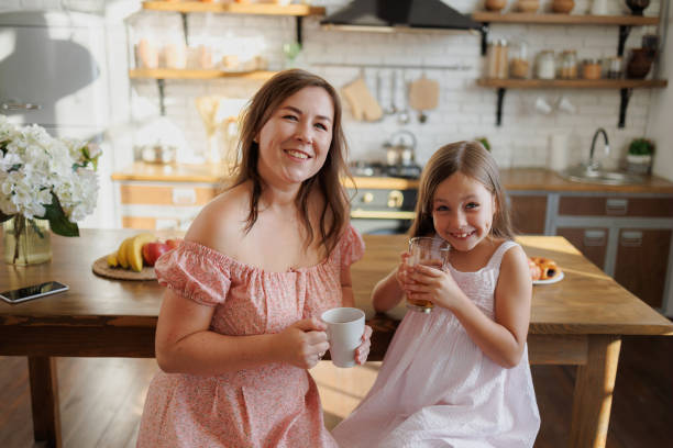 istock Smiling mother and kid in sundress holding drinks in kitchen 2168013310