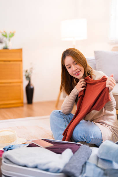 istock A young woman is sitting on the floor, checking off items on a packing list while organizing her suitcase for a trip, ensuring everything is in order 2168013695