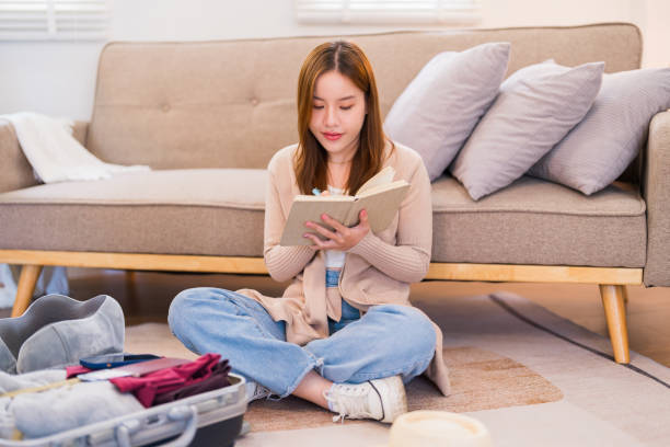 istock A young woman is sitting on the floor, checking off items on a packing list while organizing her suitcase for a trip, ensuring everything is in order 2168013787