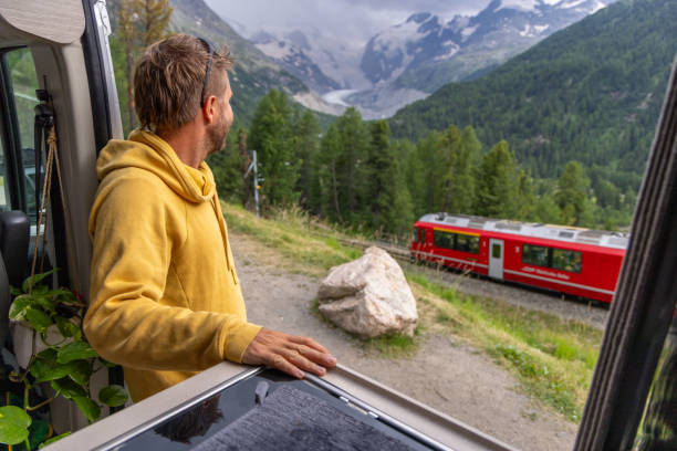istock Man Observing Passing Train from Camper Van in Mountain Landscape 2168014384