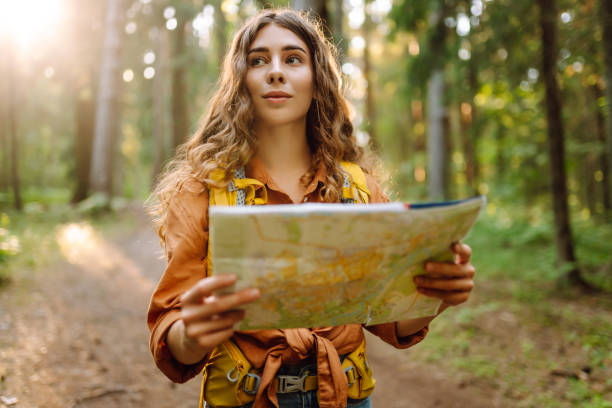 A young woman explores a forest while reading a map in the sunlight, enjoying a beautiful day outdoors.