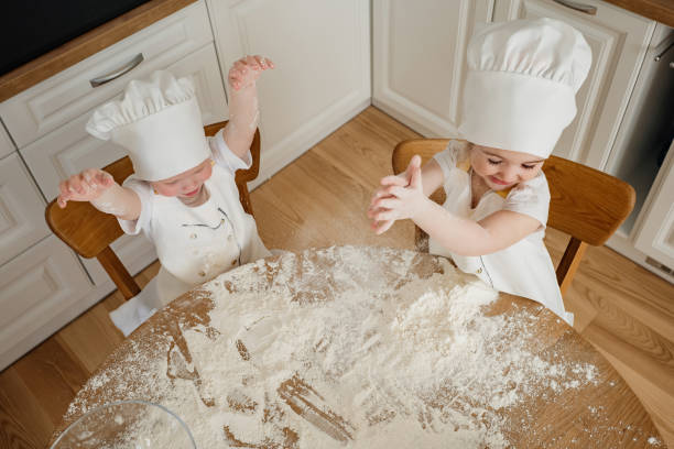 istock Two kids in chef hats play with flour at a kitchen table during a fun baking activity 2168015574