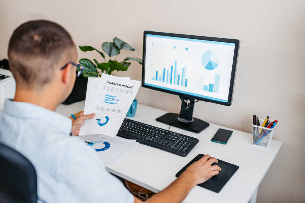 istock Mid-Adult Man Going Over Paper Documents While Working On A Computer At The Office 2168017292