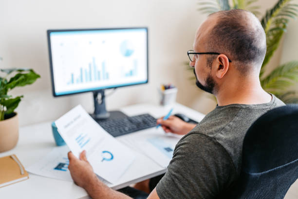istock Mid-Adult Man Going Over Paper Documents While Working On A Computer At The Office 2168017476