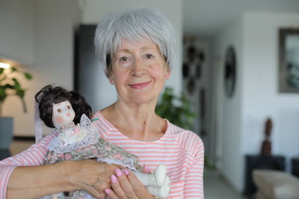 A gray haired Caucasian senior woman is holding an interesting porcelain doll. The doll has pale complexion and could be really creepy.