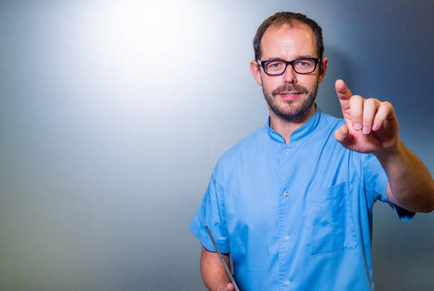 A healthcare professional wearing a blue uniform is confidently pointing towards the camera while holding a tablet. The image conveys a sense of engagement and interaction, suggesting themes of digital healthcare, patient communication, and professional expertise. The neutral background focuses attention on the professional, making it ideal for concepts related to modern healthcare services and technology