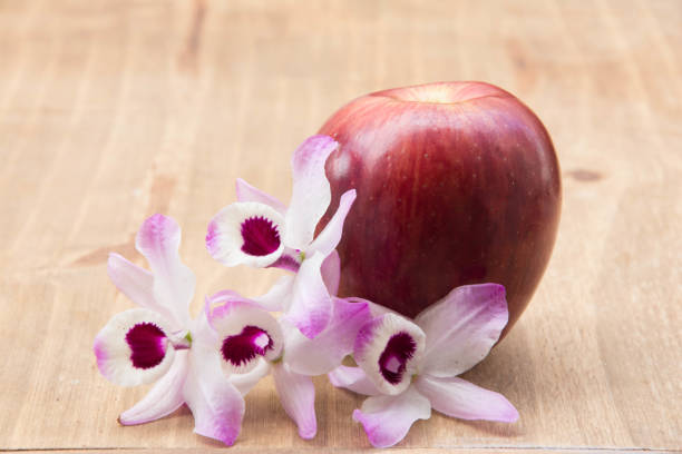 Red apple and orchid on wooden background. Healthy food concept.