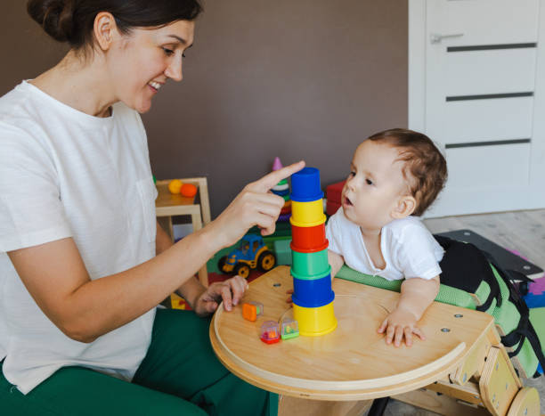 istock Cute little boy with hypotonia interacts with sensory therapist, focused on stacking colorful cups into pyramid for improved motor skills and engagement 2168049255
