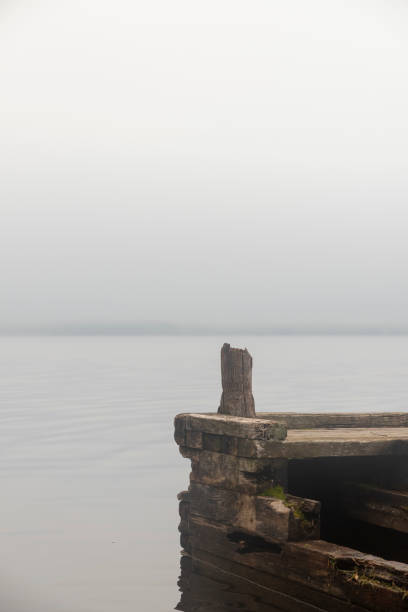 Young sad lonely woman standing on the river dock on a misty autumn day.