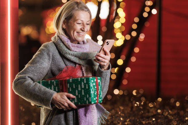 istock Smiling woman with gift box using smart phone during holiday season 2168051092