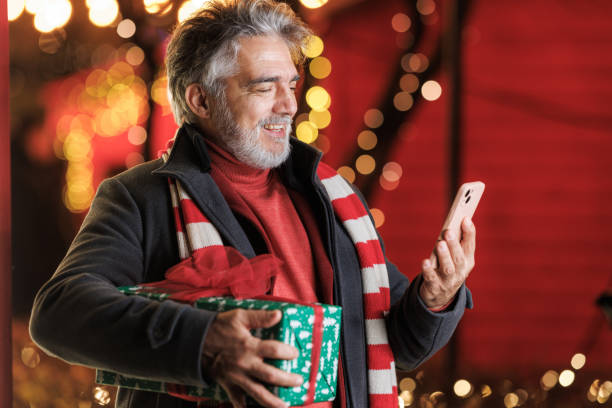 istock Joyful senior man with gift using smart phone outdoors at Christmas 2168051100