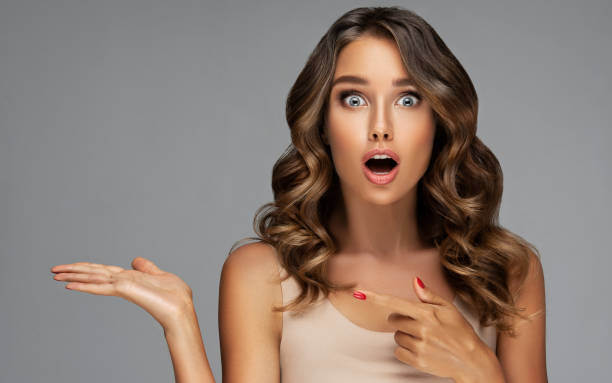 istock Young beautiful long haired model with surprised fecial expression is pointing aside. Makeup Hairstyle Human emotion. 2168055364