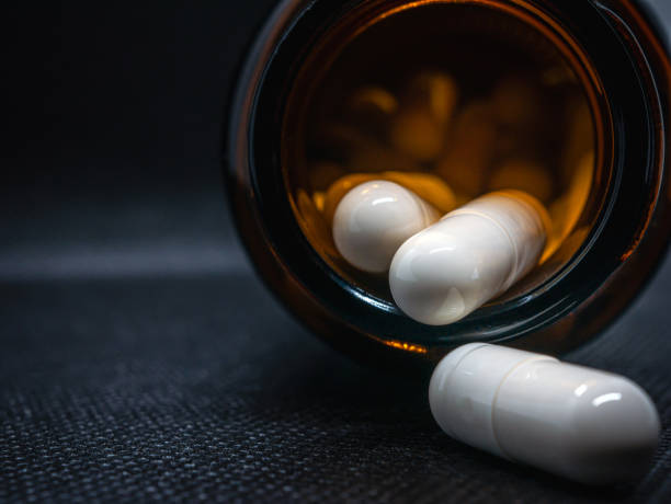Close-up of white pills capsules spilling out of pill bottle on black. White pills capsules medicine or vitamin capsules, macro stock photo