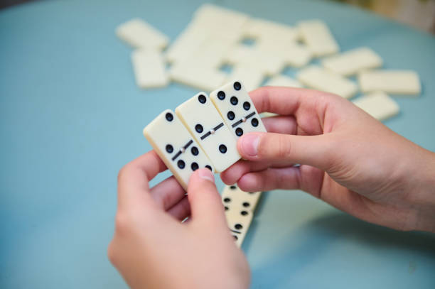 istock Hands holding white domino tiles during a strategic board game session on a blue table background 2168059020