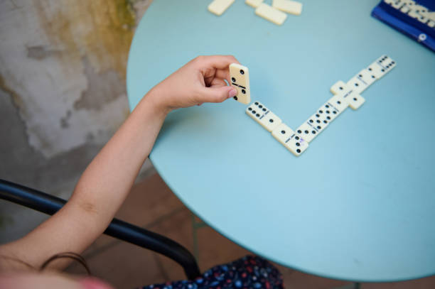 istock Child playing dominoes at a round blue table outdoors, developing strategic thinking and motor skills while enjoying leisure time in a casual setting on a sunny day. 2168059067