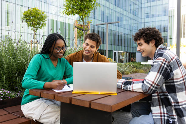 istock Happy multiracial university students studying and doing homework together outdoor college campus using laptop. 2168059377