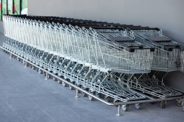 A row of shopping carts are lined up against a wall. The carts are silver and black