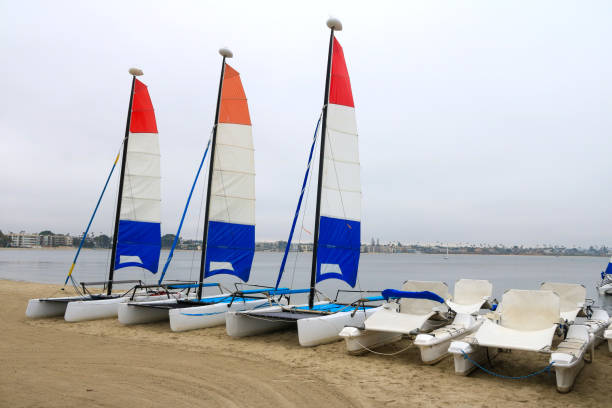 Boats float peacefully on calm blue sea, surrounded by scattered orange buoys. Rocky island and soft clouds frame tranquil maritime scene under a bright sky. Wide view of deep blue sea with sailboats