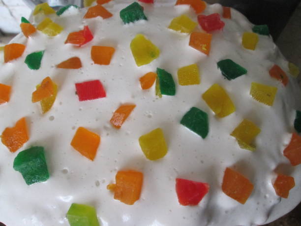 A colorful dessert showcases a fluffy white frosting layer generously decorated with vibrant jelly pieces in various shapes and colors, served in a warm kitchen ambiance.