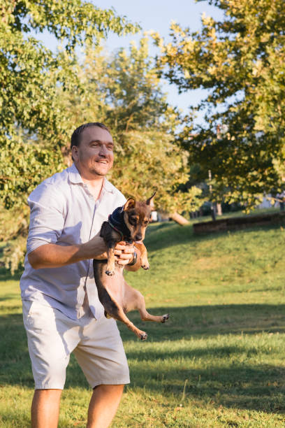 istock Smiling middle-aged man walks and plays with a small dog in public park 2168070046