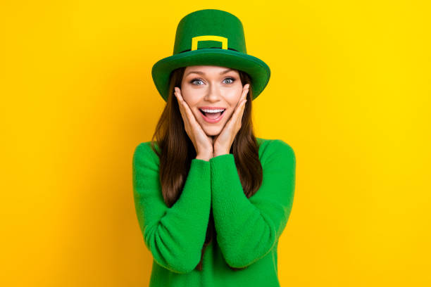 Photo of cute impressed lady dressed green pullover headwear arms cheeks celebrate patrick day isolated yellow color background.