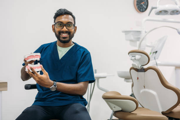 Portrait of a confident Asian dentist in a dental clinic holding artificial jaws in his hand.
