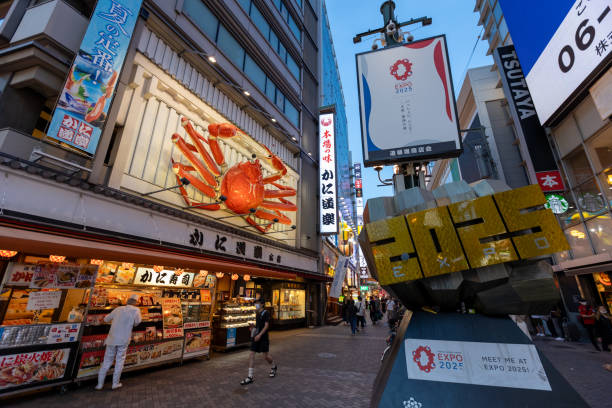 Osaka, Japan - August 19, 2022 :  People at the Dotonbori area of Osaka walking past a promotional sign for the 2025 World Expo in Osaka, Japan.