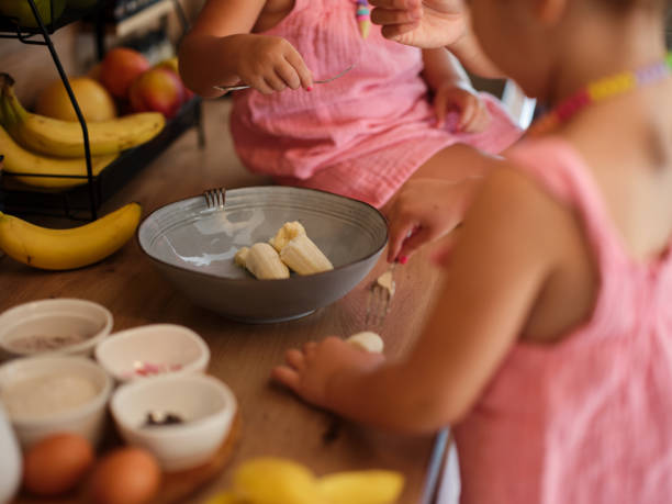 istock Two sisters in aprons delight in preparing a meal with bananas, eggs, and various ingredients under their mother's attentiveness, showcasing a joyful and educational cooking activity. 2168097020