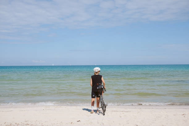 istock Young woman walks on beach with bicycle 2168101892