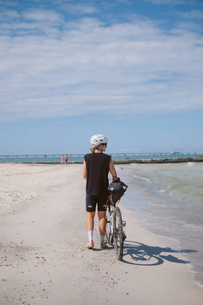 istock Young woman walks on beach with bicycle 2168101952