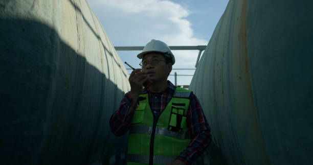 istock Senior maintenance engineer wearing a reflective vest and using a walkie-talkie while working with a blueprint drawing at a large water tank in a construction site of the factory. 2168105087