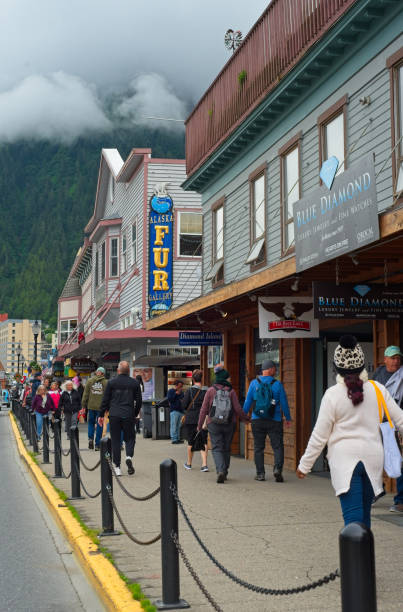 Juneau, AK, USA - June 24, 2024: Tourists crowd the sidewalk along South Franklin St. near the cruise ship piers in Alaska's capital under low-hanging clouds on a summer day.