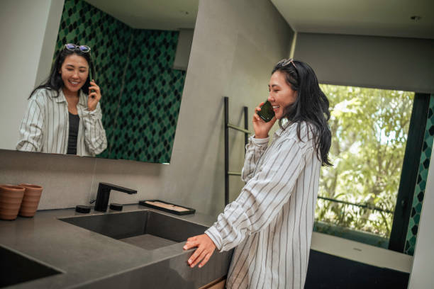 istock Joyful Asian Woman on Phone Call in Modern Bathroom 2168107008