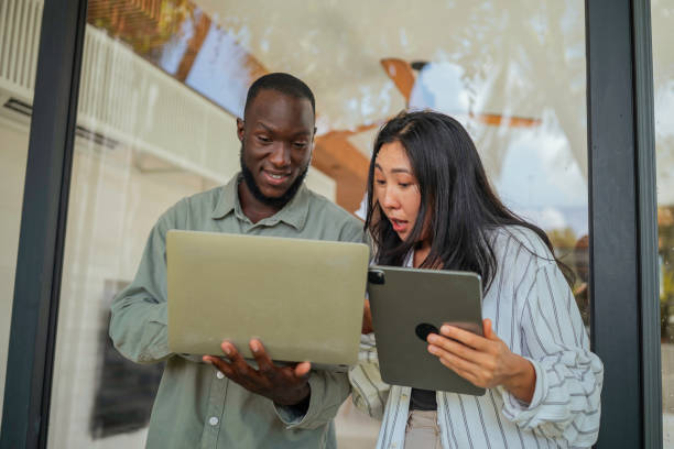 istock Cheerful Black Man and Asian Woman Collaborating with Tech Gadgets Indoors 2168107041